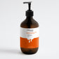 Brown bottle with pump and orange and white label on a light gray background